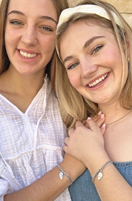 Two women smiling and wearing charm bracelets.